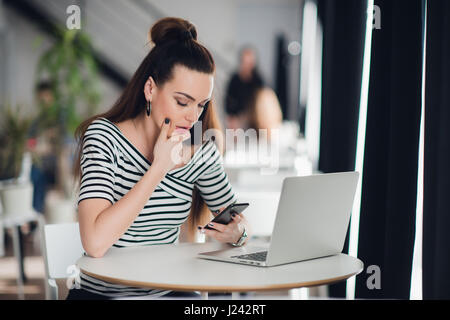 Besorgt, Vorstand im Gespräch am Telefon versucht, Probleme mit mehreren Geräten in einem Desktop im Café sitzen zu lösen. Stockfoto