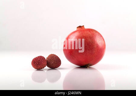 Granatapfel mit zwei kleinen Litschis auf weißem Hintergrund Stockfoto