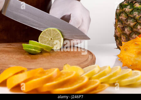 Küchenchef, schneiden Kalk auf einem Holzbrett unter den Früchten Stockfoto