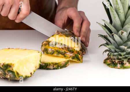 Nahaufnahme des Mannes Hände slicing frischen Ananas auf einer weißen Fläche Stockfoto
