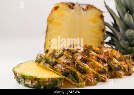 Close-up Schuss von Hälfte der Ananas und Scheiben davon auf einem weißen Hintergrund platziert Stockfoto
