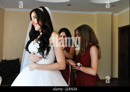 Glücklich fröhlich Brünette Braut trägt in ihrem Zimmer mit zwei Brautjungfern auf roten Kleid. Stockfoto