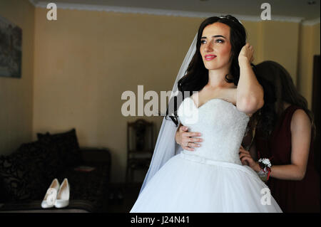 Glücklich fröhlich Brünette Braut trägt in ihrem Zimmer mit zwei Brautjungfern auf roten Kleid. Stockfoto