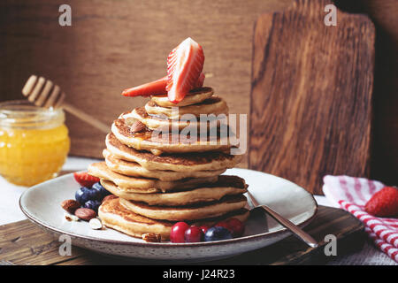 Gesunder Dinkel Vollkorn-Pfannkuchen mit Honig, Erdbeeren, Heidelbeeren und Nüssen auf einem Teller. Getönten Bild, Nahaufnahme Stockfoto