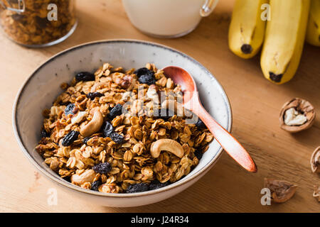 Müsli mit Rosinen und Nüssen in Schüssel geben. Frühstück mit Müsli Banane auf Holztisch Stockfoto