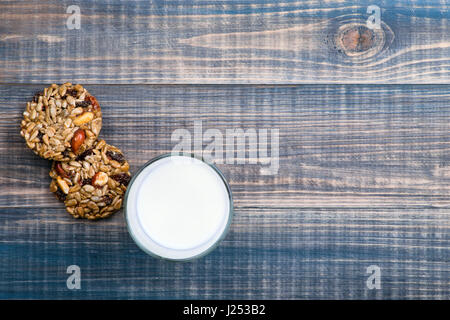 Hausgemachte Süssigkeiten aus Samen, Nüssen, Rosinen und Honig zusammen mit einem Glas Milch auf einem Holztisch. Ansicht von oben Stockfoto