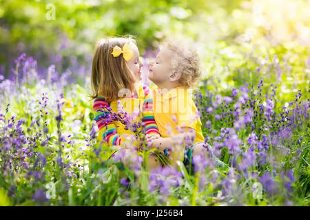 Kinder mit Bluebell Blumen. Jungen und Mädchen im Garten. Kinder spielen im Freien in Glockenblumen Wiese. Bruder und Schwester arbeiten im Garten, Pflanzen und Wasser Stockfoto