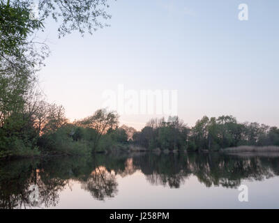 Sonnenuntergang über einem See als die Bäume um spiegeln sich im Wasser im Frühling auf dem Lande Stockfoto