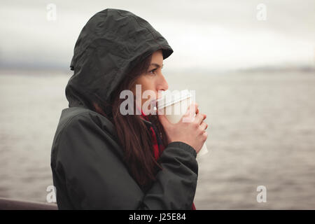 Seitenansicht der Frau trinkt Kaffee im stehen gegen Meer Stockfoto