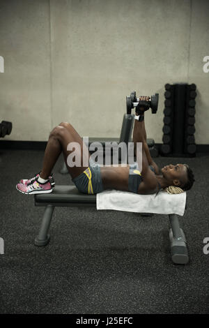 Fit Woman Training mit Kurzhanteln auf einer Bank in der Turnhalle Stockfoto