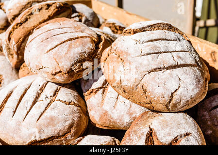 Haufen mit neu Steinofen gebackene Brote von Sauerteig-Brot mit viel Mehl obenauf liegen im Freien in der Sonne in Holzkiste. Stockfoto