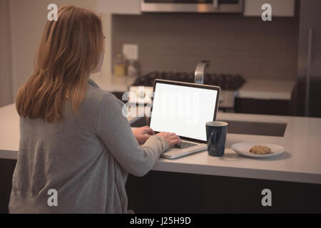 Rückansicht des Frau mit Laptop bei Kücheninsel zu Hause Stockfoto