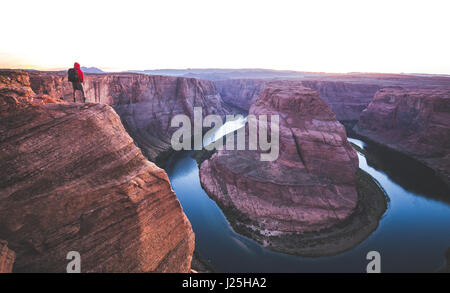 Ein männlicher Wanderer steht auf steilen Klippen, genießen die schöne Aussicht des Colorado River fließt bei berühmten Horseshoe Bend bei Sonnenuntergang, Page, Arizona, USA Stockfoto