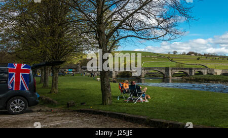 Typisch britisch: Paar mit Union Jack-Flagge auf Auto und Bulldog von ihren Füßen mit Liegestühlen - schöne Yorkshire Dales Dorf Burnsall, UK Stockfoto