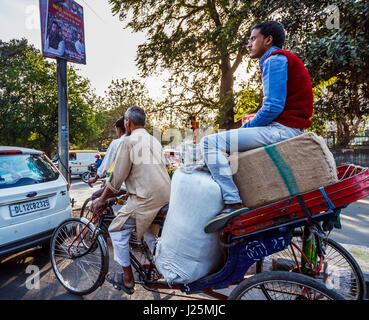 Lokalen indischen Mann treten eine Dreirad-Rikscha, Passagier sitzt auf eine große Last von Säcken an einer Straßenkreuzung in einer belebten Straße in Alt-Delhi, Indien Stockfoto