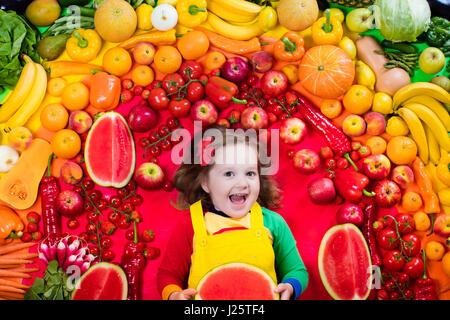 Kleines Mädchen mit Vielzahl von Obst und Gemüse. Bunte Regenbogen von rohem Obst und Gemüse. Kind, gesunden Snack zu essen. Vegetarische Ernährung Stockfoto