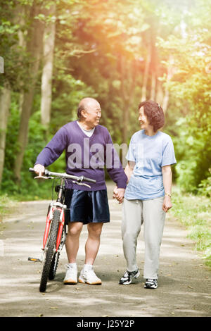 Ein paar ältere asiatische sprechen beim gehen und trainieren in einem park Stockfoto