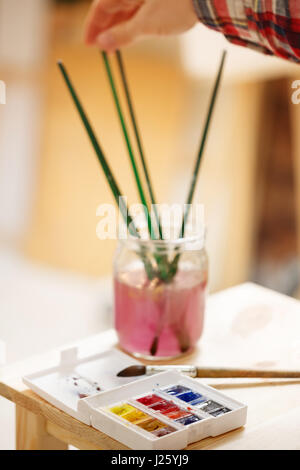 Pinsel in ein Gefäß mit Wasser. Zeichnung mit Aquarellfarben. Close-up mit Pinsel und Farben. Stockfoto