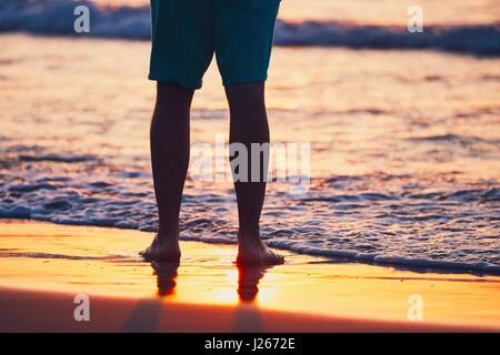 Urlaub am idyllischen Strand. Die Beine des jungen Mannes in traumhaften Sonnenuntergang. Stockfoto