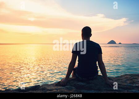 Betrachtung auf den wunderschönen Sonnenuntergang. Silhouette des jungen Mannes am Strand. Stockfoto