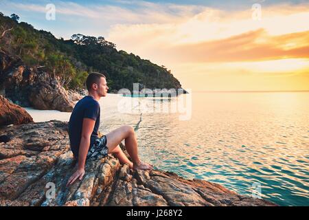 Betrachtung auf den Sonnenuntergang. Allein junger Mann am schönen Sandstrand. Stockfoto