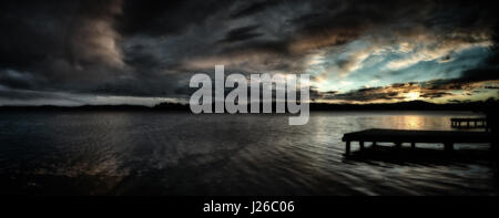 Sonnenuntergang über dem Lago di Varese mit dramatische Wolken in den Himmel und Pier im Vordergrund, Herbstsaison Stockfoto