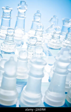 Nahaufnahme von mattierten und klaren Schachfiguren aus Glas auf einem blauen Schachbrett aus Glas, von oben aus einem diagonalen Winkel betrachtet Stockfoto