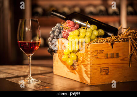 Zusammensetzung der Obst-Kiste, Flasche Wein und Weinglas platziert auf einem Holztisch in einem Weinkeller. Stockfoto