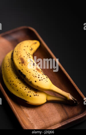 Zwei Bio-Bananen in einem Holz über ein schwarzes Brett. Stockfoto