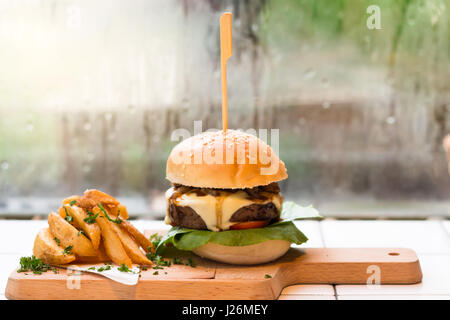 Hausgemachte Hamburger mit Rindfleisch, Salat, Käse, Tomaten und Kartoffeln Pommes Frites auf Tablett aus Holz. Stockfoto