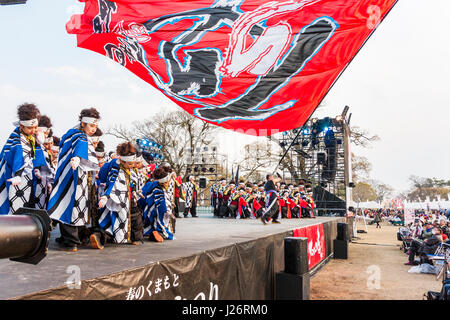 Hinokuni Yosakoi Dance Festival. Team von jugendlichen Frauen tanzen auf der Bühne und trug gemusterten happi Mäntel. Massive rote Flagge geschwenkt werden über asudience. Stockfoto