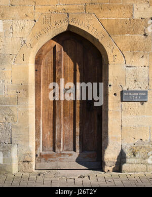 Altes Gymnasium Holztür und Inschrift [Scholae Grammatica] in den Steinbogen gehauen. Chipping Campden, Cotswolds, Gloucestershire, England Stockfoto