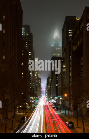 Die Aussicht von Tudor Stadt in Richtung das Chrysler Building bei Nacht, die teilweise in der Wolke ist, Auto Licht Wanderwege auf der Straße gesehen werden kann, Neue Stockfoto