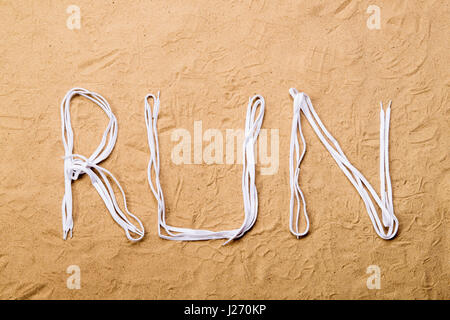 Laufen Sie Zeichen der Schnürsenkel, Sand Hintergrund. Flach zu legen. Stockfoto