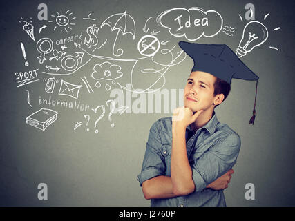 Schöner junger Mann mit Graduierung Hut nachschlagen Nachdenken über Bildung hat viele Ideen über das zukünftige Leben auf graue Wand Hintergrund isoliert Stockfoto