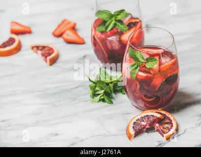 Blutorange und Erdbeere Sommer Sangria. Erfrischende Früchte stieg Wein Cocktails im Glas mit Eiswürfeln und frische Minzblätter über Marmor Tisch bac Stockfoto