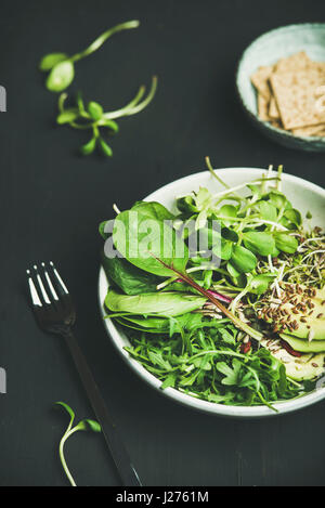 Grüne Vegan Frühstück Mahlzeit in Schüssel mit Spinat, Rucola, Avocado, Samen und Sprossen auf schwarzem Hintergrund, selektiven Fokus. Sauber, Essen, Diät, ve Stockfoto