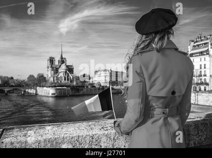 Hell in Paris. Hinter modernen Reisenden Frau im roten Mantel am Ufer in der Nähe von Notre Dame de Paris in Paris, Frankreich mit französischen Flagge gesehen Stockfoto