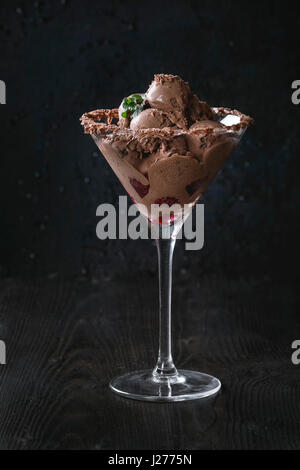 Cocktailglas mit Mini Kugeln Schokoladeneis mit frischen Himbeeren und Minze auf schwarzen verbrannten Holz Hintergrund. Stockfoto