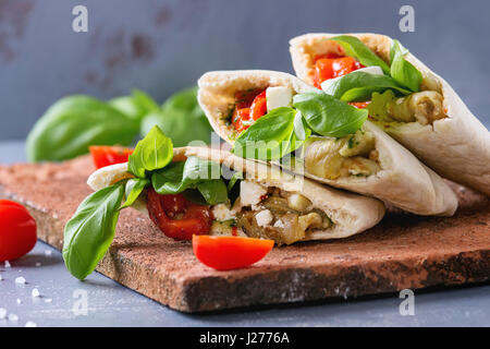 Pita Brot Brötchen mit gegrilltem Gemüse Paprika, Auberginen, Tomaten, Basilikum und Feta-Käse auf Terrakotta über grauen Stein Hintergrund serviert. Stockfoto