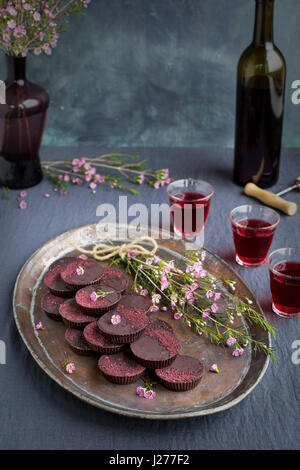 Marzipan-Hibiscus-Tassen serviert auf einem Kupfertablett mit Dessertwein. Phototgraphed auf eine graue Tischdecke. Stockfoto