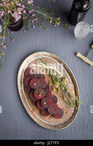 Marzipan-Hibiscus-Tassen serviert auf einem Kupfertablett mit Dessertwein. Phototgraphed auf eine graue Tischdecke. Stockfoto