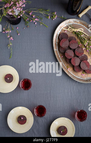 Marzipan-Hibiscus-Tassen serviert auf einem Kupfertablett mit Dessertwein. Phototgraphed auf eine graue Tischdecke. Stockfoto