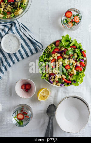 Erdbeere Nudelsalat mit Kräutern und Gurke in einer Schüssel und begleitet von zwei Glas aromatisiertes Wasser und Schalen. Stockfoto