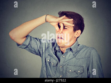 Mann drückt Nase mit den Fingern sieht mit Ekel etwas schlechten Geruch auf grauem Hintergrund isoliert stinkt. Menschliches Gesicht Ausdruck Körpersprache Reaktion Stockfoto