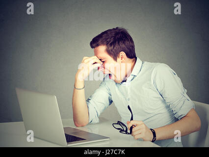 Erschöpft. Müde junger Mann geschlossen massieren seine Nase und Augen sitzend an seinem Arbeitsplatz vor Laptopcomputer Stockfoto