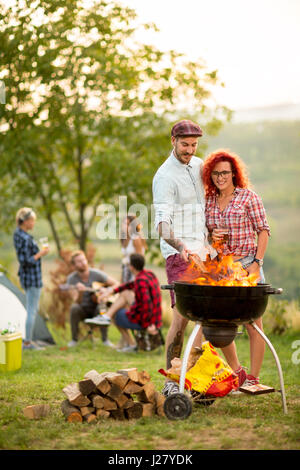 Guy Grill Feuer Protokoll aufsetzen und umarmen Sie lockiges Mädchen in Campingplatz Stockfoto