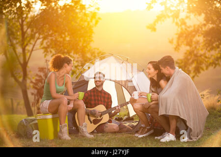 Lächelnde Gruppe von jungen Camper genießen in der Musik der Gitarre Stockfoto