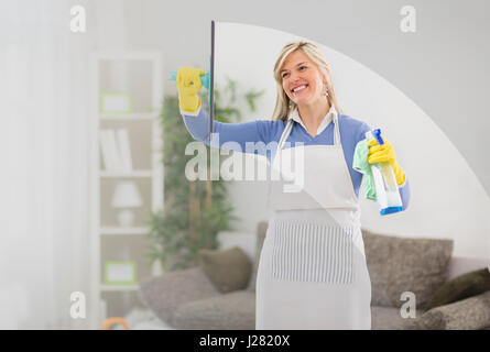 Lächelnde Frau reinigt Fenster im Haus Stockfoto
