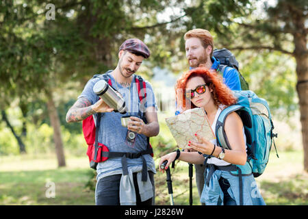 Sportlerinnen und Sportlern Wandern mit Rucksack, Karte, Thermoskanne und Wanderstöcke durch Wald Stockfoto